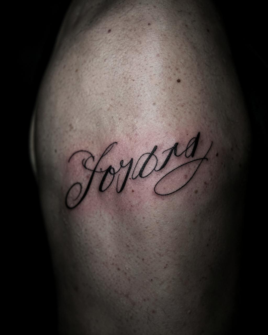 Fine line script lettering tattoo on an upper arm