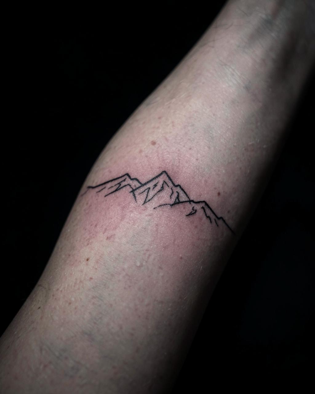 Small fine line mountain range tattoo on a forearm