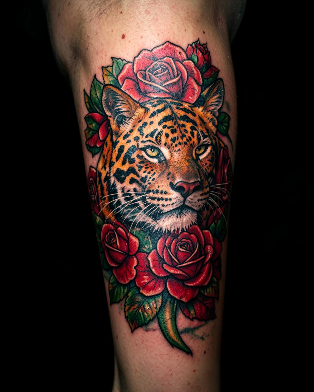 Color tattoo of a big cat surrounded by roses on a calf